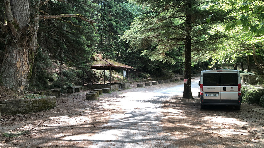 Vehicles parked at the side of a forest road in Manganiari, with a hut opposite.