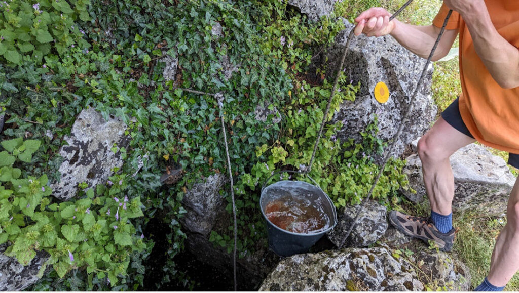 Hippocrene spring: bucket full of water being pulled up from gap in the rocks.