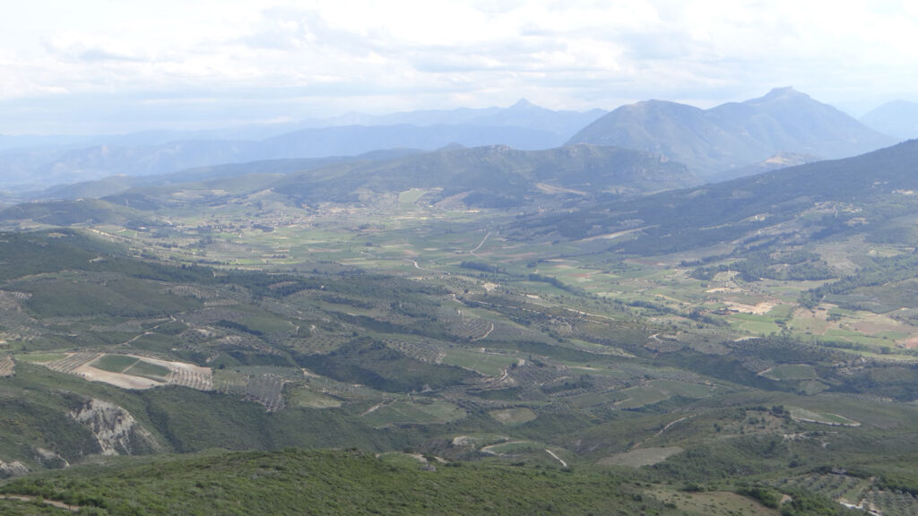View from above: plain in foreground, mountains in background, including the triangular peak of Mount Artemisio standing up above others in the distance.