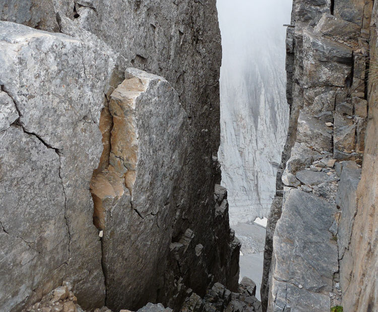 Gap between rocks, with cloud and views to distant cliff face below.