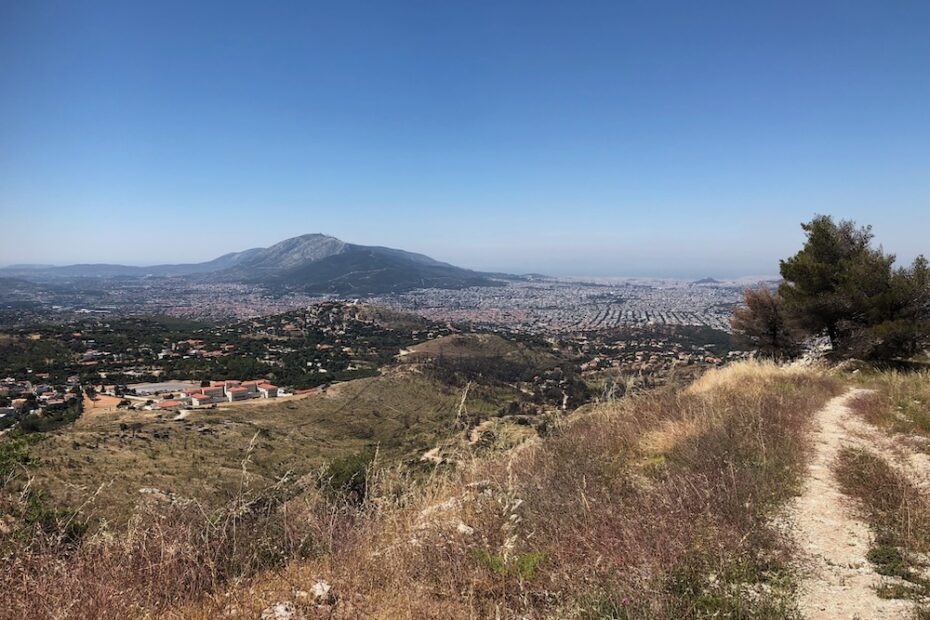 Mountain path in foreground; distant view of city and mountain in the background.