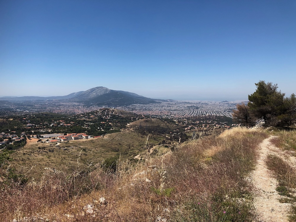 Mountain path in foreground; distant view of city and mountain in the background.