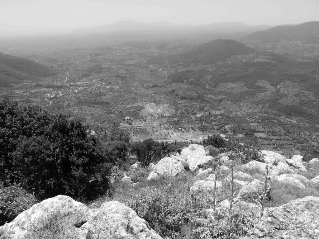 View of plains from mountaintop, with archaeological site in the distance.