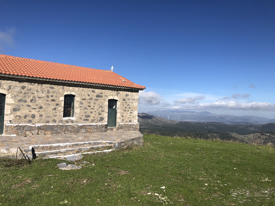 Mountaintop chapel with orange-tiled roof and mountains in the distance behind.
